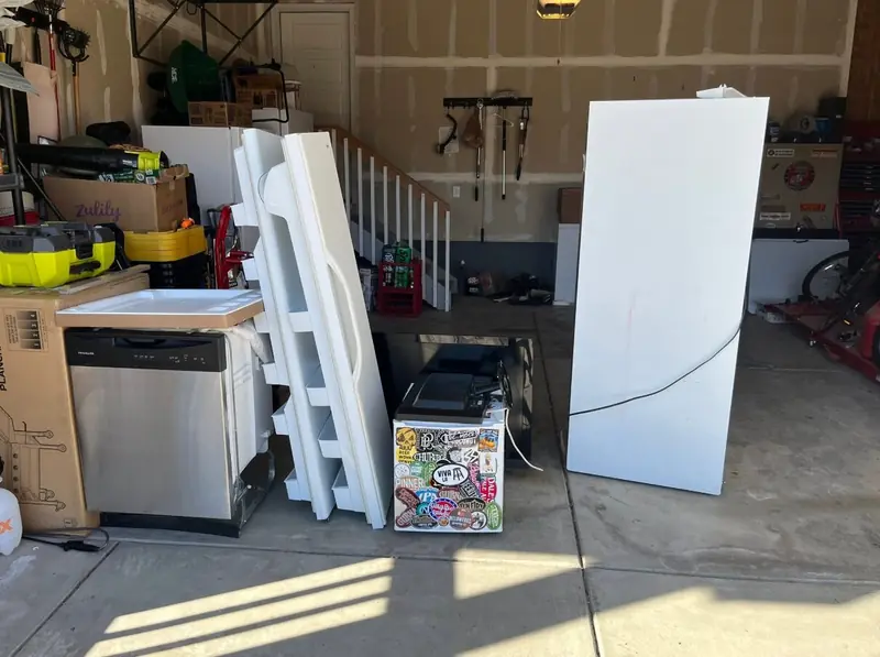 Before appliance pickup with a refrigerator, dishwasher and removed refrigerator doors ready in a garage