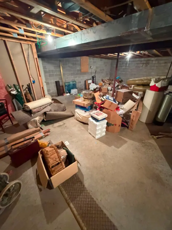 Large basement filled with boxes and furniture before cleanout