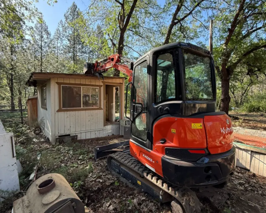Small outbuilding during demolition with a compact excavator