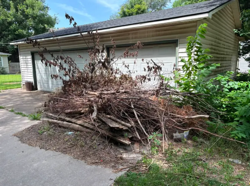 Large pile of branches beside a garage before removal
